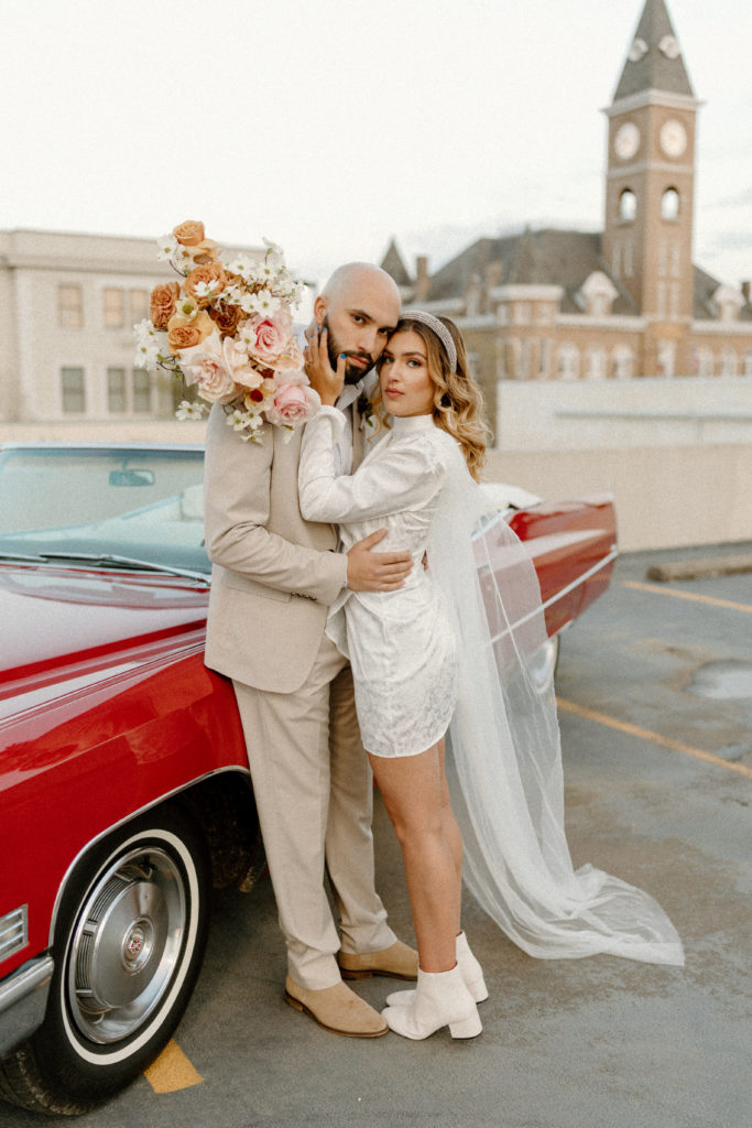 bride and groom embracing with classic car in background-- best arkansas elopement locations