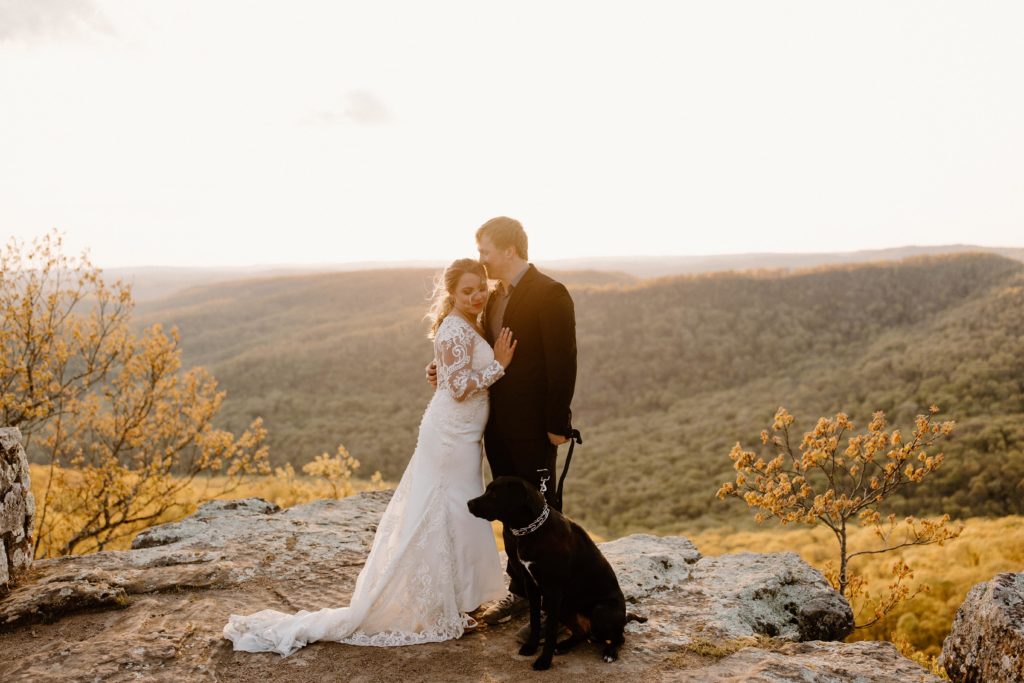 bride and groom and dog embrace on scenic overlook-- best arkansas elopement locations, white rock elopement, buffalo river elopement, arkansas elopement