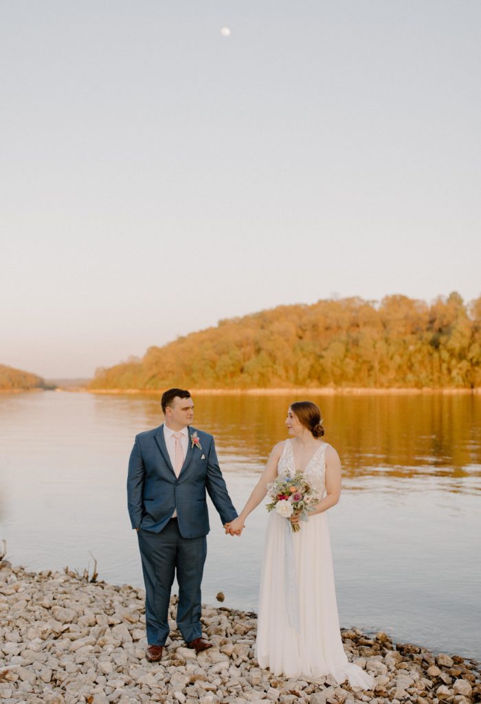 bride and groom holding hands beside sunlit lake-- best arkansas elopement locations