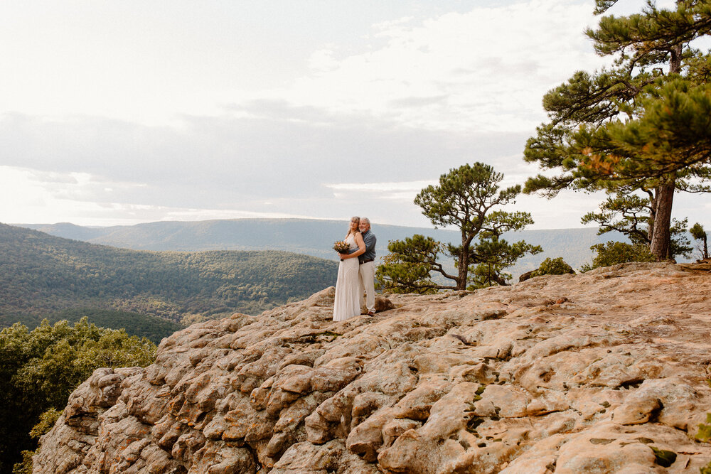 a couple holding each other close while looking off into the scenic view atop a mountain -- sams throne wedding arkansas