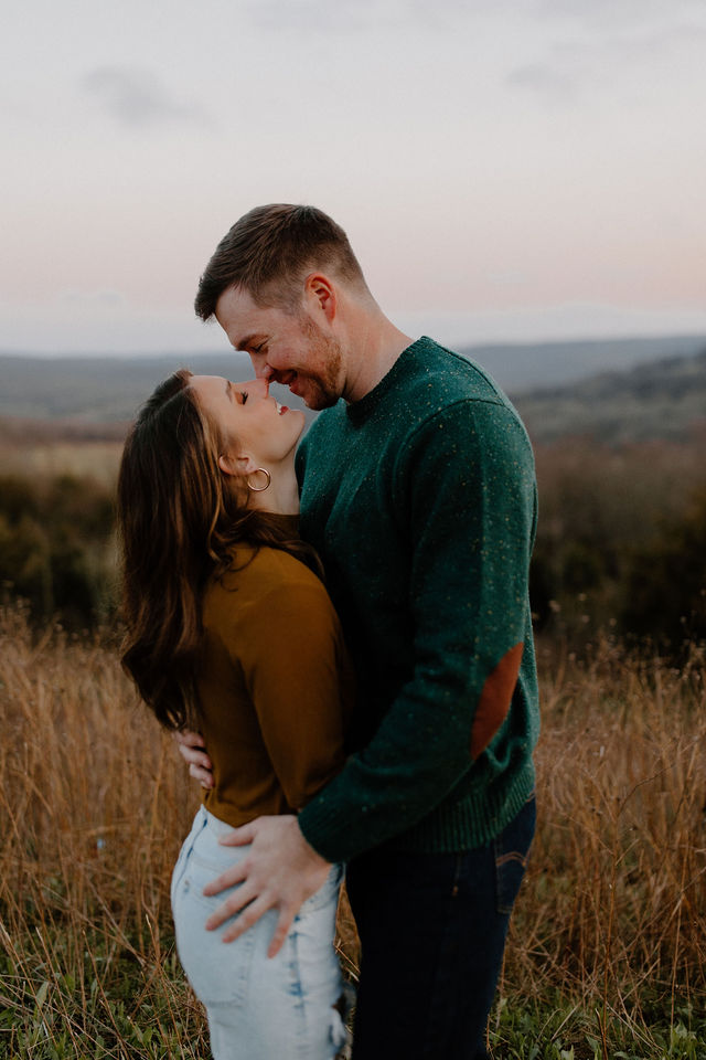 man and woman touching noses and smiling in field -- devils den engagement photo session