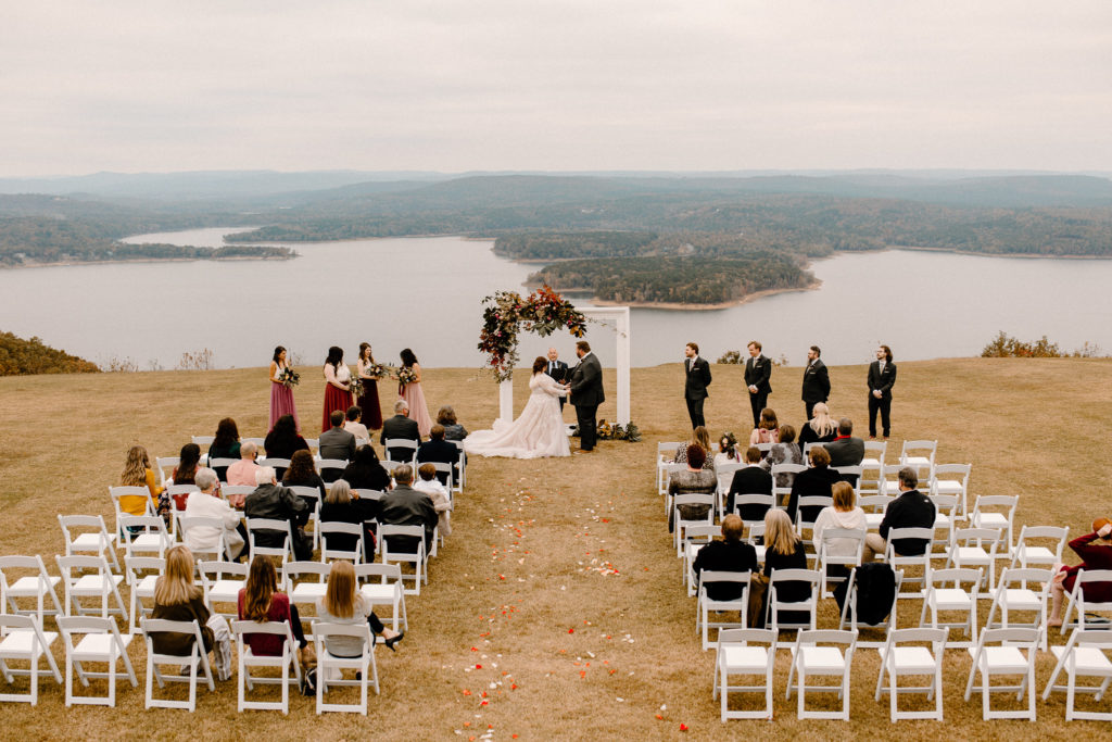 bride and groom mid-ceremony holding hands over lakeside view -- arkansas wedding photographer