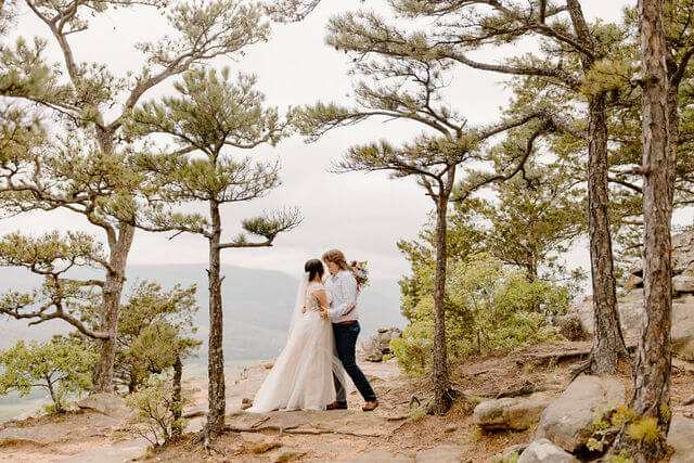 a couple holds on to one another with pine trees around them -- arkansas elopement sams throne